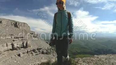 一个带着<strong>双肩包</strong>和太阳镜的微笑的旅游女孩带着她的相机走在一个岩石高原的边缘